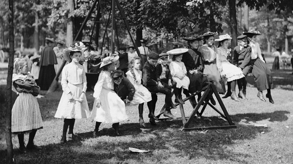 black and white photo of children sitting on a seesaw in a park