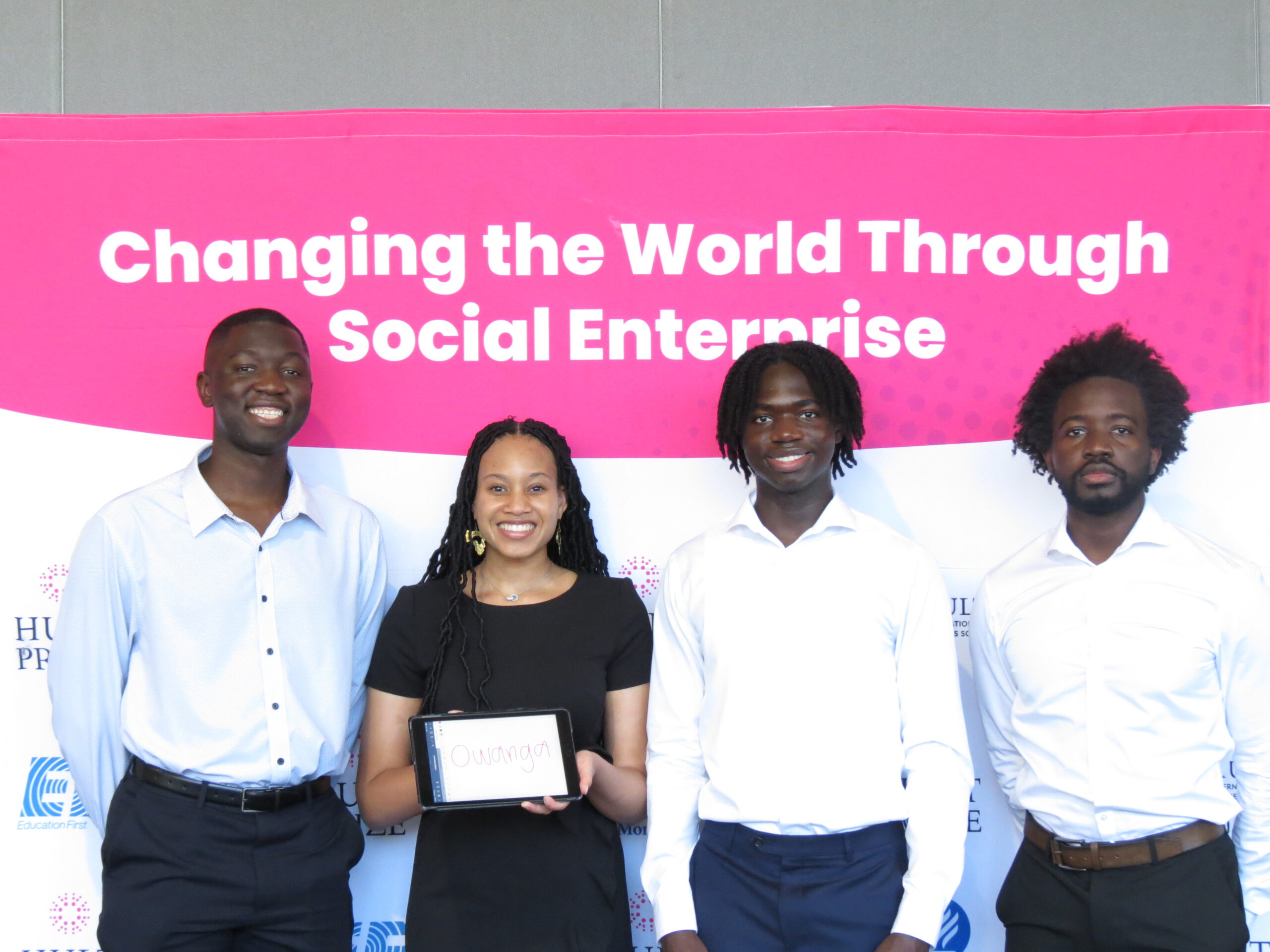 Four students stand before a banner reading "Changing the World Through Social Enterprise."