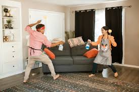 a man and woman play fighting with cleaning supplies in a living room