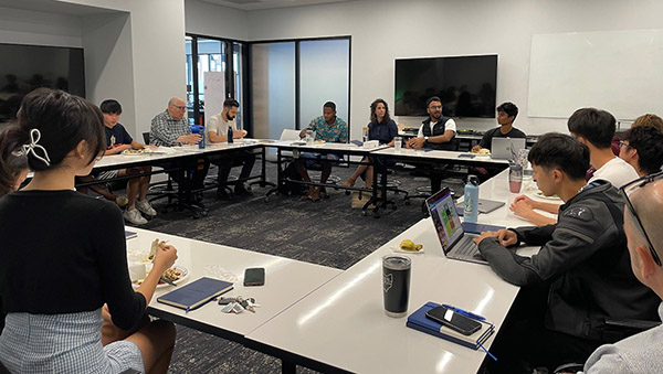 Students and Hatchery staff are in sitting in a white room with hollow square table arrangment, listening to founders Shashwat Murarka and Alissa Cohan Allen.